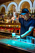 Young Asian bartender pouring rum in the glass while preparing mojito cocktail in the bar
