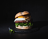 Tasty burger with egg placed on patty and fresh lettuce served on slate board on black background in studio