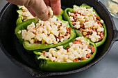 Crop anonymous person adding cheese on green bell peppers with pizza stuffing in frying pan during cooking process in kitchen