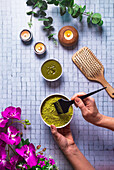 Top view composition with crop anonymous female master with bowl of died powdered henna near brush wooden comb and burning candles for natural hair care