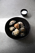 Top view of bowl with uncooked clams and salt placed on gray tabletop during food preparation