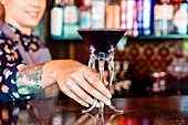 Anonymous smiling female barkeeper standing at bar counter with a type of alcohol drink served in creative cocktail glasses in shape of jellyfish
