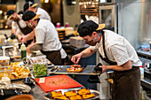 Männlicher Koch, der eine Füllung auf ein Fladenbrot auf einem rostfreien Tablett aufträgt, in Schutzmaske und Uniform in einem Restaurant