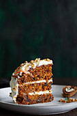 Yummy cake with cream cheese served on plate with fresh carrot slices and walnuts