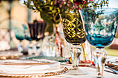 Close-up of served festive table with crystal glasses cutlery napkin on plate near bunch of fresh flowers for wedding