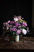Strauß frischer bunter Pfingstrosen und Chrysanthemen in weißer Vase auf Holztisch in dunklem Raum
