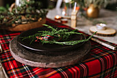 From above Christmas table setting with wreath on ceramic plate on red checkered tablecloth on the background