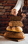 Crop anonymous female baker demonstrating soft fresh bread with crunchy seeds at table in bakery