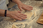 From above of crop unrecognizable elderly cook rolling out crust on table with flour while cooking in kitchen at home