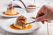 Crop unrecognizable female eating sweet egg custard with dulce de leche on white plate served on wooden table in kitchen