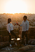 Seitenansicht eines Paares mit Bier, das sich bei Sonnenuntergang auf einem Balkon in Kappadokien, Türkei, ansieht