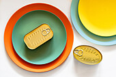 Von oben auf rechteckige geschlossene Blechdose auf grünen und orangefarbenen runden Tellern auf weißem Tisch platziert