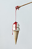 Wooden dipper with berry sauce pouring on waffle cone with yummy vanilla ice cream levitating against gray background