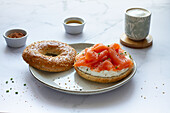 Frischer Bagel mit Käse und Lachs auf einem Teller, serviert auf einem Tisch mit einer Tasse heißem Kaffee in einer hellen Küche
