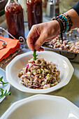 Anonymer männlicher Koch serviert appetitlichen Salat auf einem Teller, der auf einem Tisch mit verschiedenen Gerichten in der Küche steht