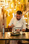 Bearded professional male chef preparing ingredient for sea urchin on plate at table in modern restaurant
