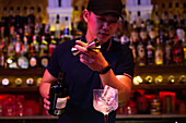 Young Asian bartender pouring gin from the jigger to the glass for preparing a gin tonic cocktail in the bar