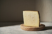 Triangle piece of delicious fresh hard cheese placed on wooden board on table in light studio