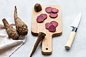 From above composition of ripe raw beetroot slices placed on wooden cutting board on kitchen table near sharp knife