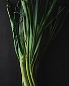 From above of fresh raw leeks with green stems placed on black surface