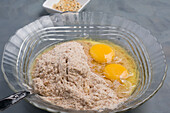 Glasschale mit Mehl und aufgeschlagenen Eiern zum Backen gesunder Bagels auf einem Tisch in einer hellen Küche während des Backvorgangs