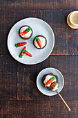 Blick von oben auf einen Teller mit leckeren Gemüse-Cupcakes mit kleinen Karotten als süße Dekoration auf einem Holztisch