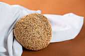 From above loaf of tasty sesame bread placed near soft white fabric on brown background