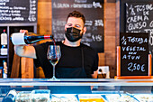 Anonymer Barkeeper gießt Wein aus einer Flasche in ein Glas am Tresen eines Restaurants mit vielen Schildern