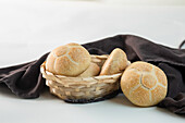 Leckere, frisch gebackene Brötchen in einer Weidenschüssel neben braunem Stoff vor weißem Hintergrund