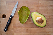 Draufsicht auf eine halbe und leere Schale einer frischen Avocado, die auf einem Schneidebrett neben einem Messer liegt