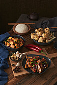 Mala tofu and yuxiang, chinese vegan dishes, accompanied by a bowl of rice, cauliflower, soy sauce and a Japanese teapot on top of a wooden table decorated with fabrics