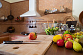 Weichzeichner einer frischen Tomate auf einem Schneidebrett mit einem Messer in der Nähe eines Straußes reifer Früchte bei der Zubereitung gesunder Lebensmittel in der Küche