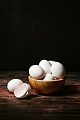 Ungekochte Eier in einer Schale auf einem Holztisch vor dunklem Hintergrund zum Frühstück