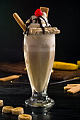 Glas süßer Bananenmilchshake, garniert mit Schlagsahne, Waffeln und Kirsche mit Schokolade obenauf