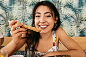 Young candid female with crunchy bread slice looking at camera in cafeteria with ornamental wall