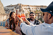 Lächelnde Freunde sitzen am Tisch und stoßen mit Cocktails an, während sie in einer Bar abhängen