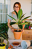 Young female florist in apron planting green plant into ceramic pot while working in professional floristry studio