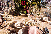 Von oben servierte festliche Tafel mit Kristallgläsern, Besteck und Serviette auf einem Teller neben einem Strauß frischer Blumen für eine Hochzeit