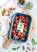 Top view of ripe cherry tomatoes with black olive slices and feta cheese in baking dish near uncooked penne