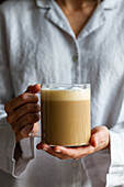 Crop unrecognizable female standing with glass cup of homemade coffee with milk for breakfast