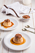 From above of egg custards topped with sweet Dulce de leche served on white plates on table with cutlery in kitchen