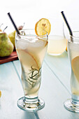 Von oben kalter Birnencocktail in Gläsern mit Rosmarin und Eiswürfeln auf einem Tisch mit frischen Früchten