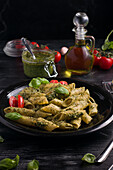 From above of plate with delicious pasta with green pesto sauce and tomatoes served on black wooden table