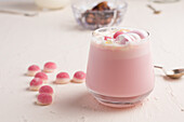 Glass of sweet hot white chocolate with pink jelly candies and marshmallow served on white table