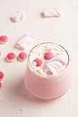 Glas mit süßer heißer weißer Schokolade mit rosa Geleebonbons und Marshmallow auf weißem Tisch