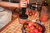 Crop anonymous housewife blending tomatoes in blender while preparing marinara sauce in kitchen at home