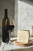 Arrangement of aromatic red wine in glass served on table near wine bottle and triangle cheese piece