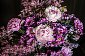 Bouquet of fresh colorful peonies and chrysanthemums in glass vase placed on wooden table in dark room