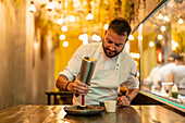 Bearded professional chef in white uniform with dispenser adding cream on portion of gourmet sea urchin in fine dish restaurant