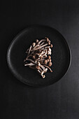 Top view of fresh shimeji mushrooms served on black plate on dark table in studio